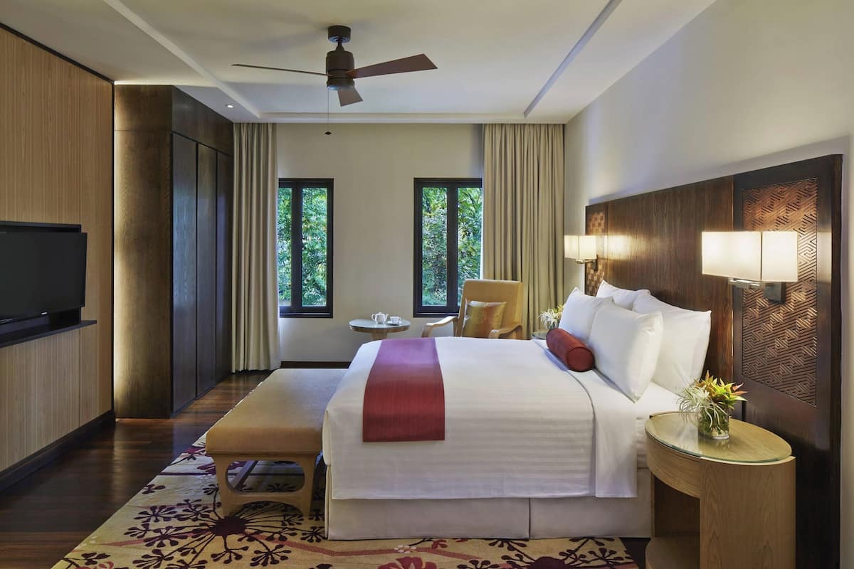 A hotel room with a bed, bedside table, lamp, TV, and a window with curtains.