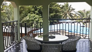 A balcony with a round table and wicker chairs, overlooking a swimming pool and lush greenery. - Quest Lodge (Accra)