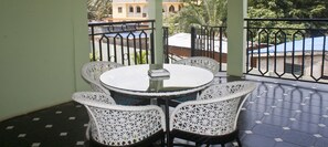 A round table with four white wicker chairs on a balcony with a tiled floor and metal railing. - Quest Lodge (Accra)
