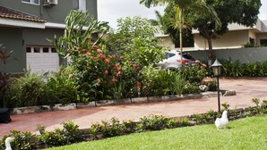 A residential area with a paved driveway, a white car parked in the driveway, and a white bird on the grass. - Quest Lodge (Accra)