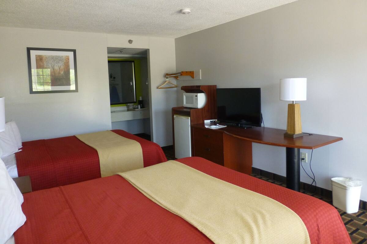 A hotel room with two beds, a desk with a television, a microwave, and a lamp.