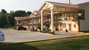 A motel with multiple balconies, a covered parking area, and a red car parked in front. - Coach Inn (Summerville)