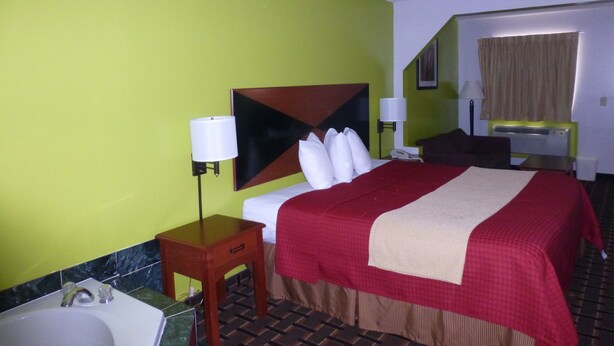 A hotel room with a bed, bedside lamps, a small wooden table, a bathroom with a sink, and a mirror. - Coach Inn (Summerville)
