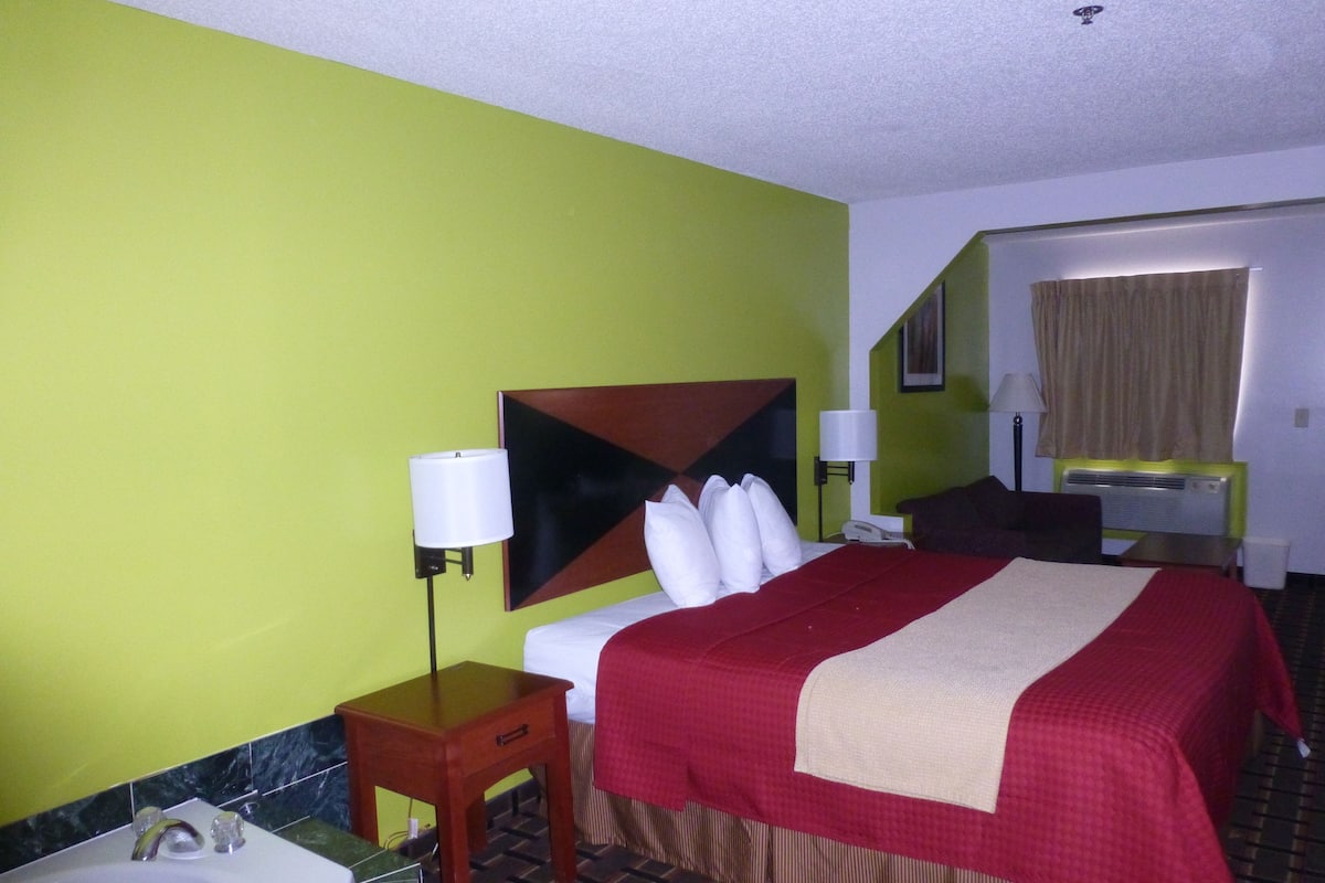 A hotel room with a bed, bedside lamps, a small wooden table, a bathroom with a sink, and a mirror.