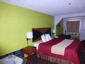 A hotel room with a bed, bedside lamps, a small wooden table, a bathroom with a sink, and a mirror. - Coach Inn (Summerville)