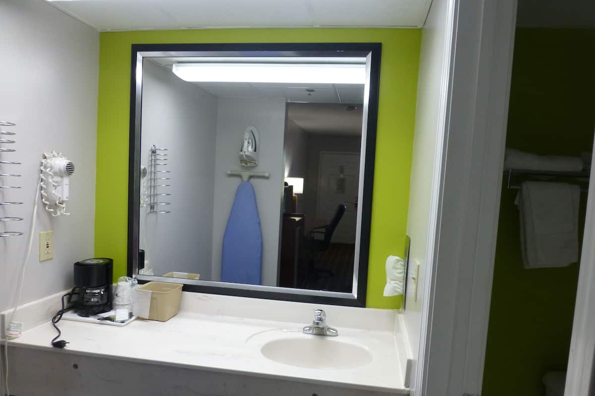 A bathroom with a white sink, a mirror, a hairdryer, and an ironing board.