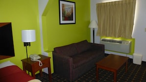 A hotel room with a green wall, a brown sofa, a wooden table, a lamp, a telephone, and an air conditioning unit. - Coach Inn (Summerville)