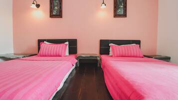 Una habitación con dos camas, cada una con una colcha rosa y almohadas a juego. Hay lámparas de pared y cuadros enmarcados sobre las camas.