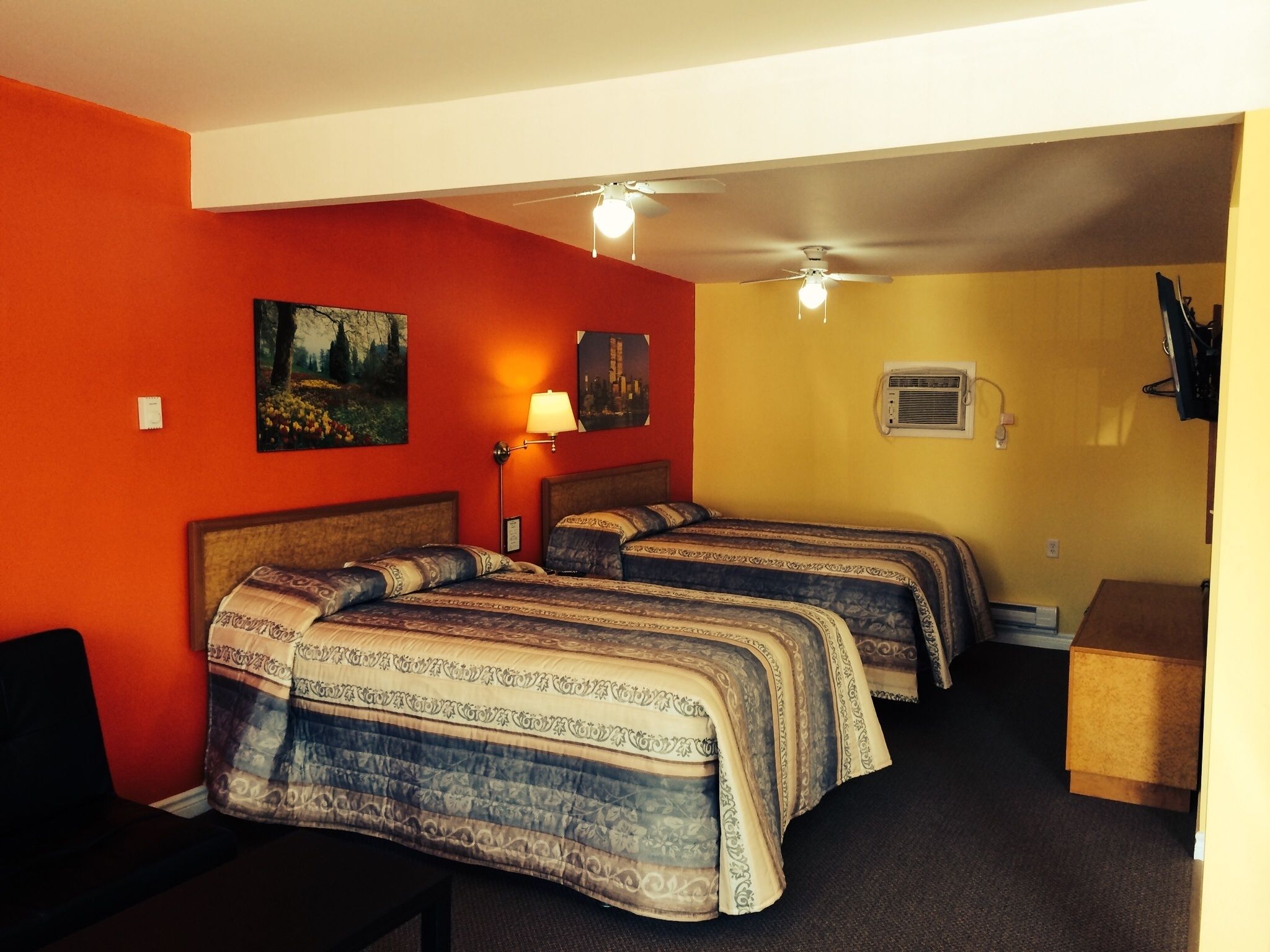 A hotel room with two beds, a ceiling fan, a wall-mounted air conditioner, and a desk with a chair.