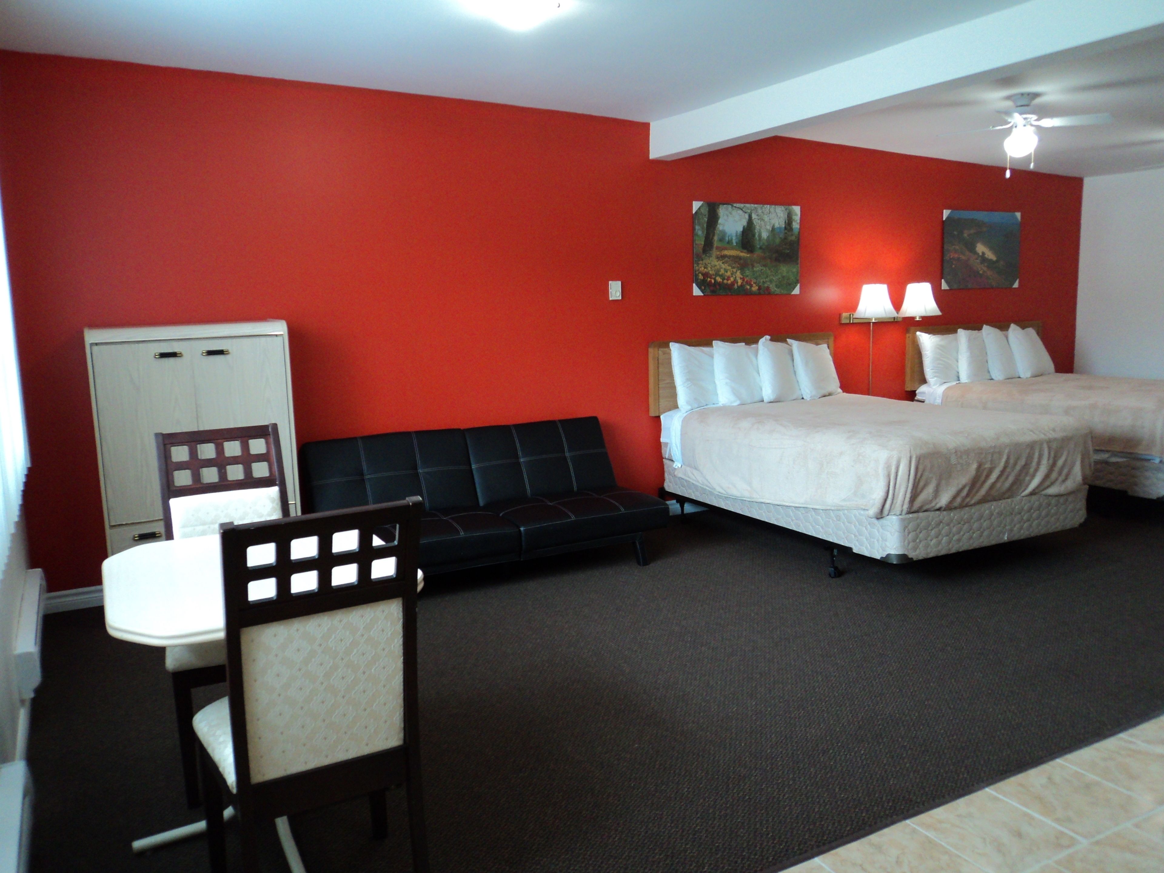 A hotel room with a red wall, two beds, a desk, and a chair.