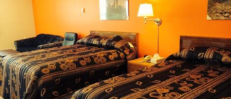 A hotel room with two beds, a desk, a chair, and a lamp.