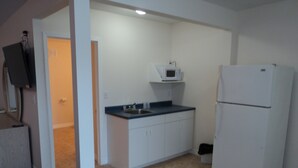 A compact kitchen with white cabinets, a built-in microwave, and a refrigerator. - Rymal's Motel (Leamington)