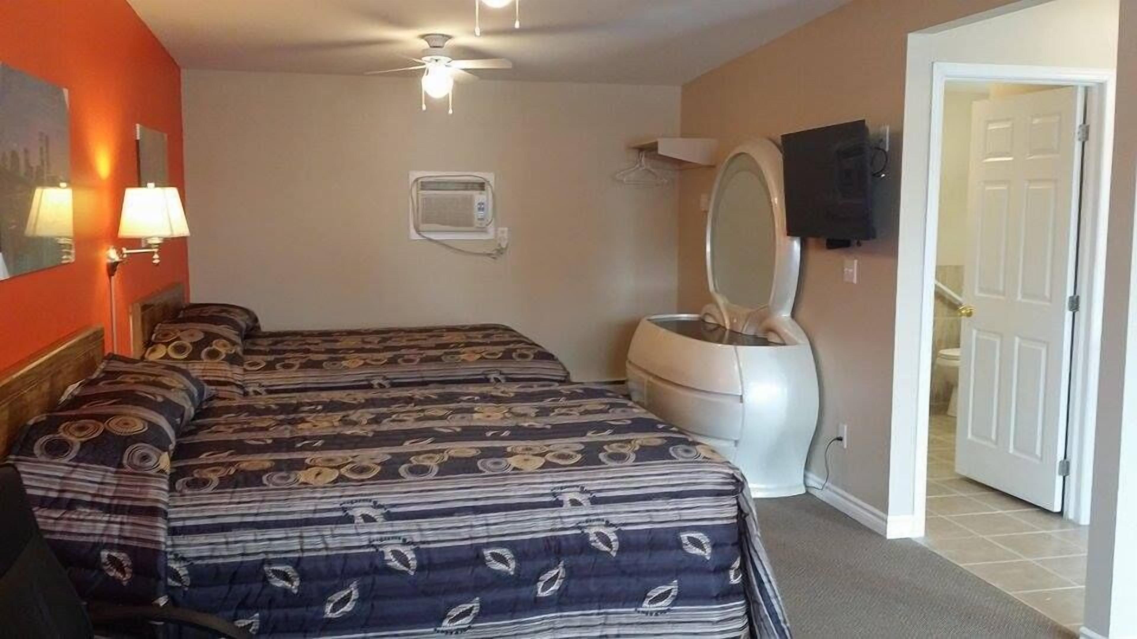 Quarto de hotel com duas camas, sanitário, televisão e ventoinha de teto.
