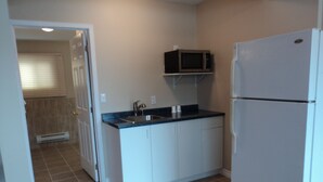 A kitchen with white cabinets, a black countertop, a microwave, and a refrigerator. - Rymal's Motel (Leamington)