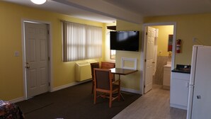 A compact living space with a dining area, a TV mounted on the wall, and a kitchen area. - Rymal's Motel (Leamington)