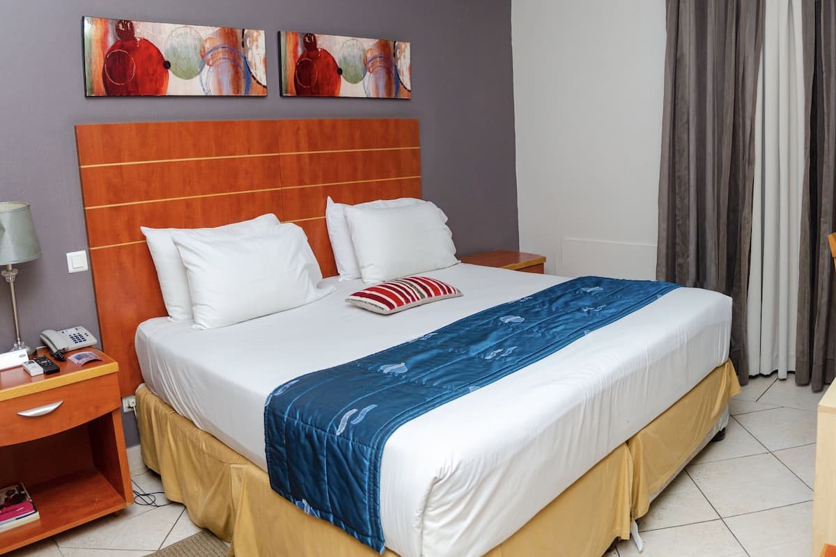 A hotel room with a bed, bedside table, lamp, and a desk with a chair.