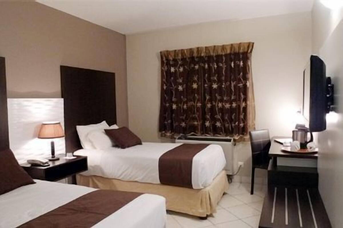 A hotel room with two beds, a desk, a chair, a TV, and a window with curtains.