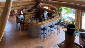 A rustic log cabin interior with a bar area, wooden beams, and large windows. - Williston Lake Resort (Hudson's Hope)