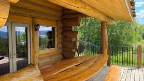 A log cabin with a wooden deck and a glass door leading to a patio. - Williston Lake Resort (Hudson's Hope)