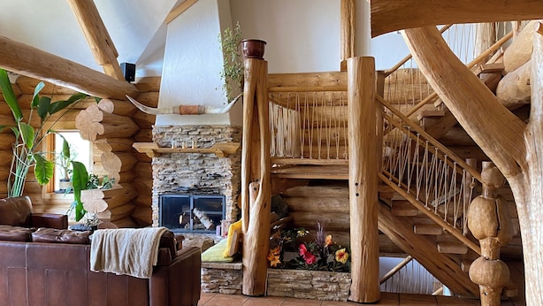 A log cabin interior with a stone fireplace, wooden staircase, and a leather sofa. - Williston Lake Resort (Hudson's Hope)