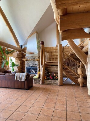 A log cabin interior with a stone fireplace, wooden staircase, and a leather sofa. - Williston Lake Resort (Hudson's Hope)