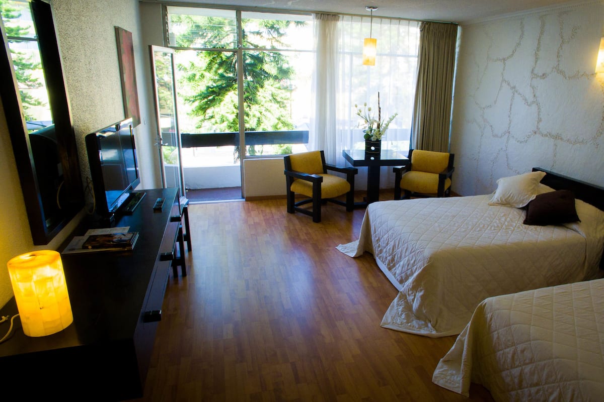 A hotel room with two beds, a desk, a chair, a TV, and a window with curtains.