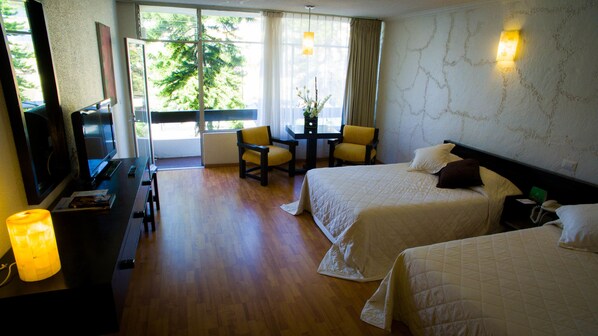 Habitación de hotel con dos camas, un escritorio, una silla, un televisor y una ventana con cortinas.