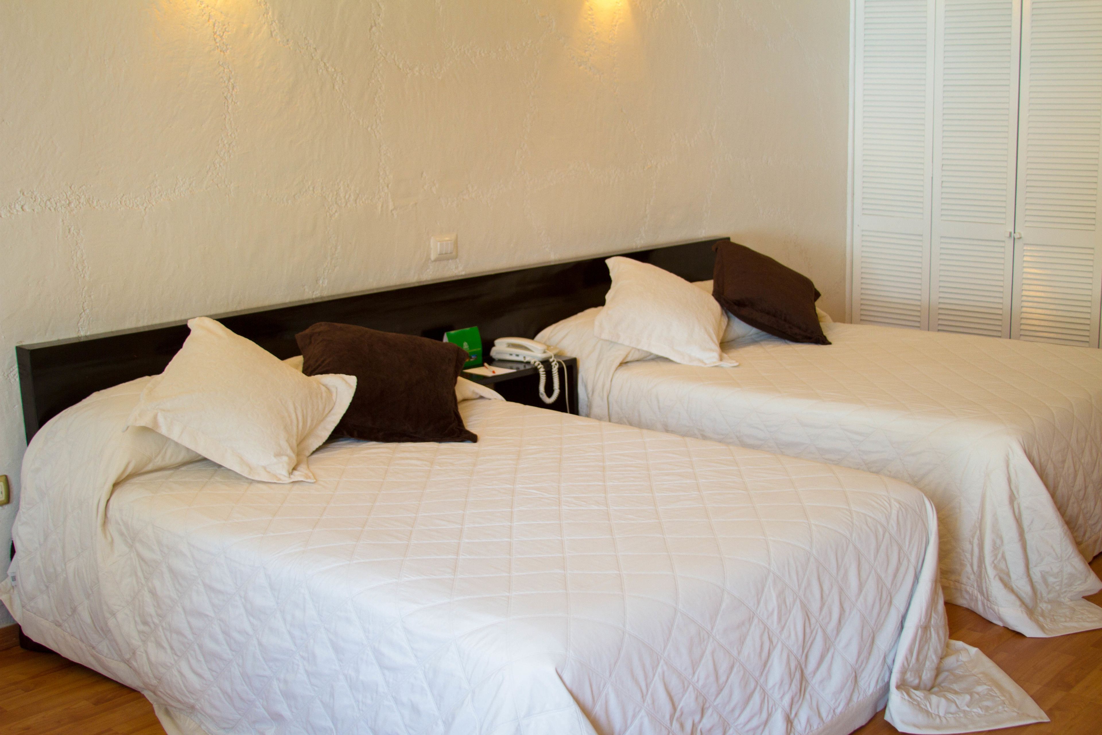 Two single beds with white bedding, a bedside table with a phone, and a wall-mounted light fixture.