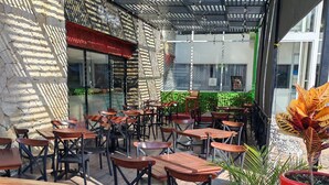 Un café al aire libre con mesas y sillas de madera, un muro de piedra y un techo de metal.
