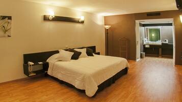 Habitación de hotel con cama, mesita de noche, lámpara y baño visible a través de una puerta abierta.