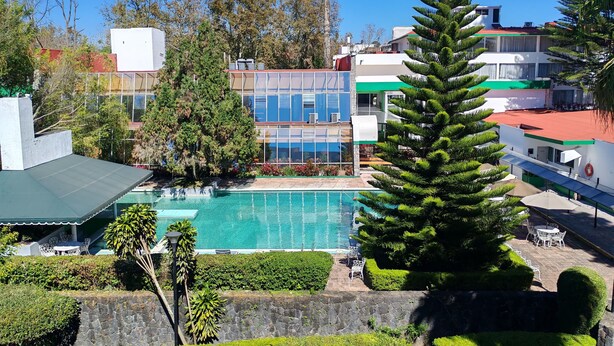 Una piscina rodeada de vegetación, edificios modernos y zonas de estar al aire libre.