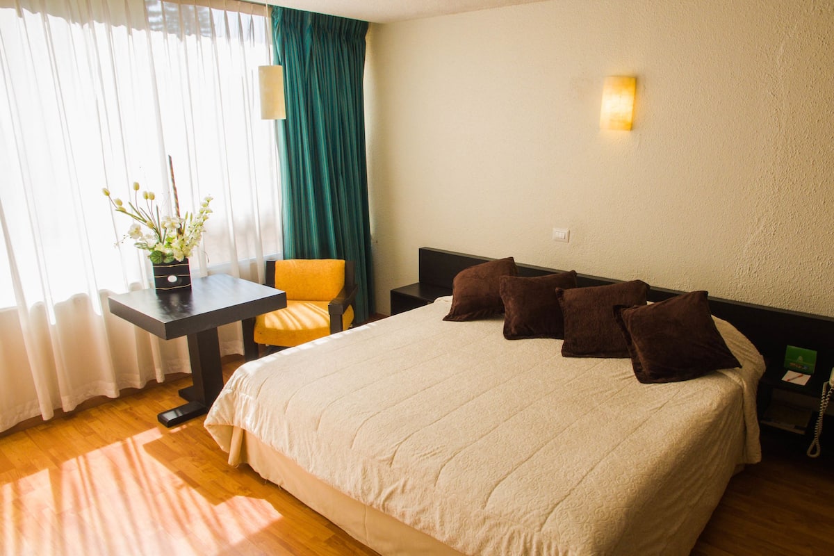A hotel room with a bed, a desk, a chair, and a telephone.