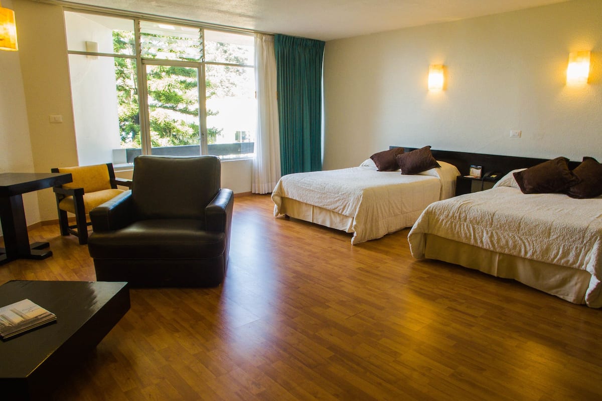 A hotel room with two beds, a chair, a table, and a window with curtains.