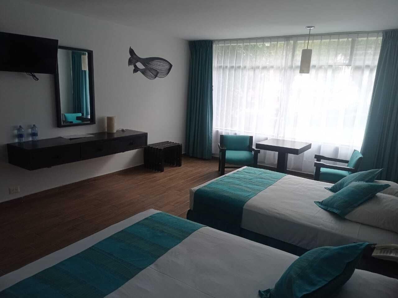 A hotel room with two beds, a desk, a chair, a TV, and a window with curtains.
