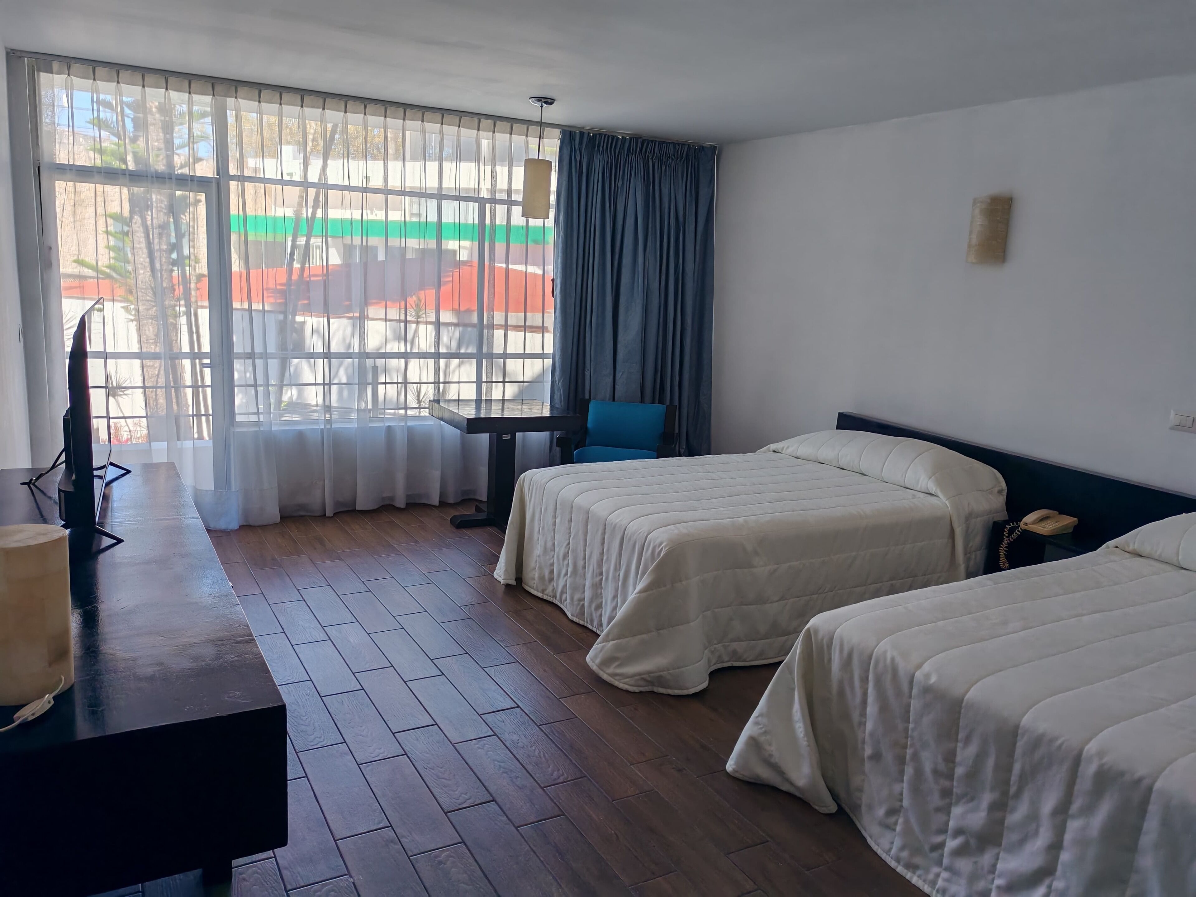 Una habitación de hotel con dos camas, un escritorio, una silla, un televisor y una ventana con cortinas.