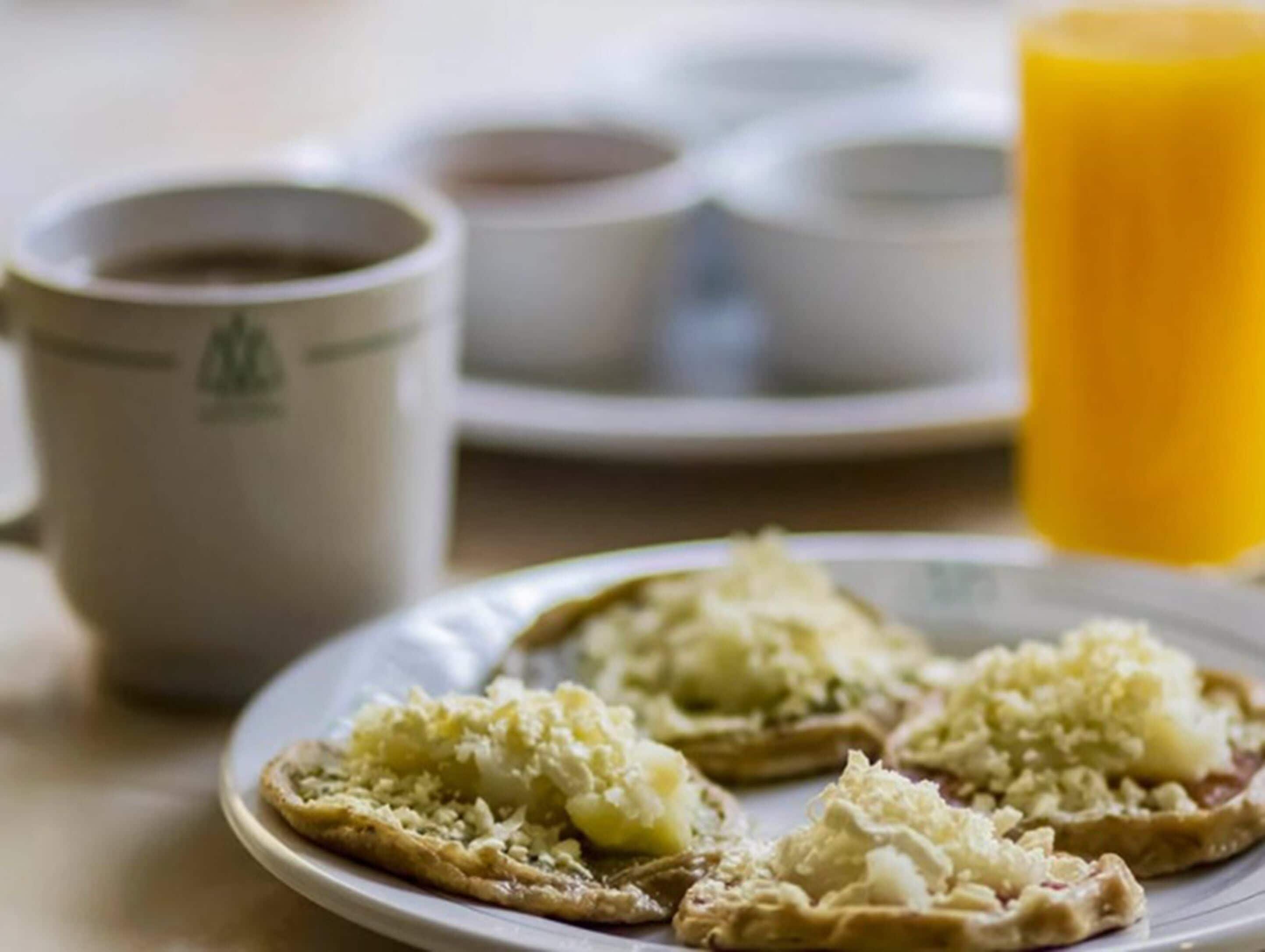 Un plato con alimentos, una taza y un vaso de zumo de naranja sobre una mesa.