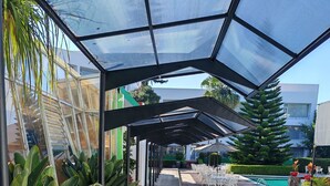 Un espacio al aire libre techado con piscina, mobiliario y plantas.