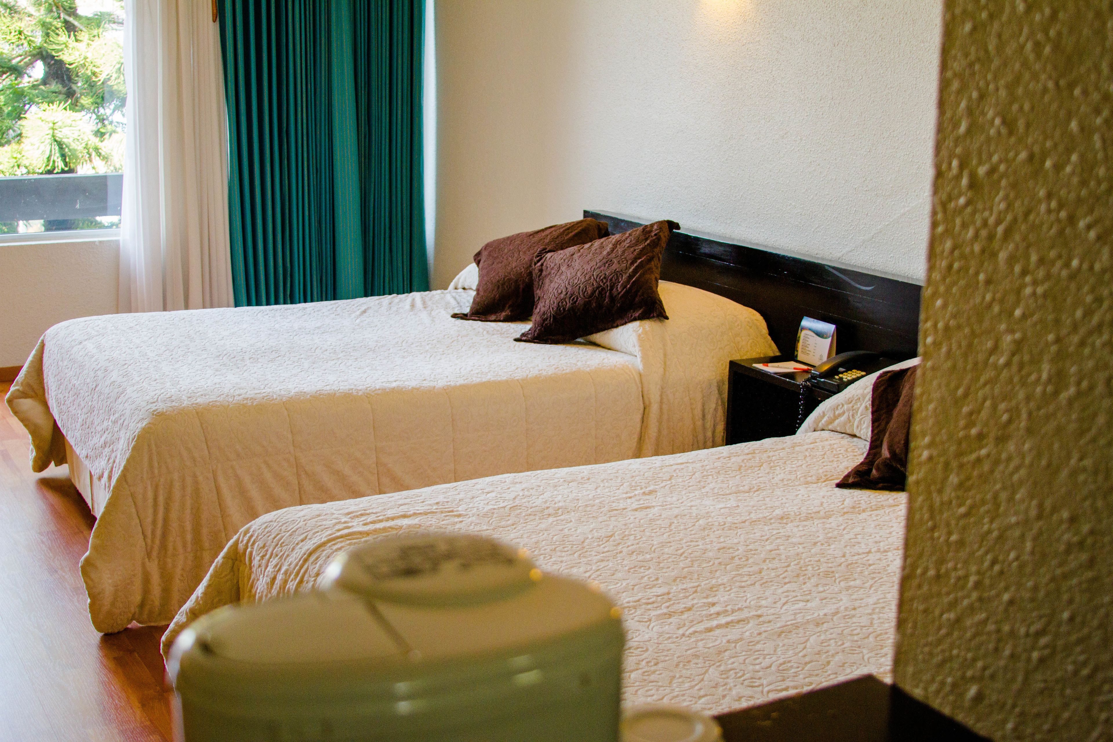 Ein Hotelzimmer mit zwei Betten, einem Nachttisch und Blick auf Grünflächen.