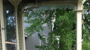A covered porch with wicker furniture, a table with a floral tablecloth, and a vase with flowers. - Hudson City Bed & Breakfast (Hudson)