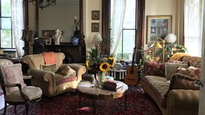 A cozy living room with a fireplace, a chandelier, a sofa, a chair, and a coffee table with books and a guitar. - Hudson City Bed & Breakfast (Hudson)