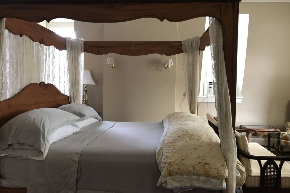 A four-poster bed with a canopy, a bedside table with a lamp, and a chair.