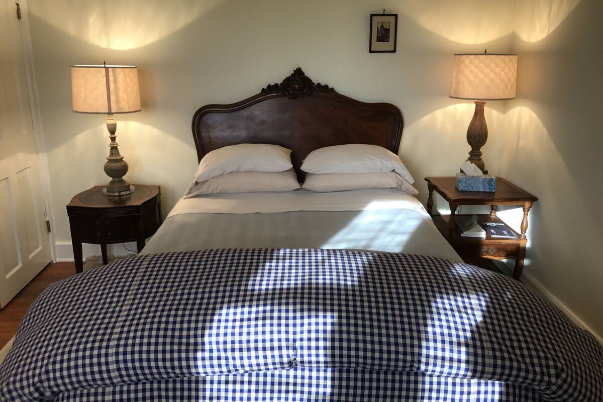 A neatly made bed with a checkered bedspread, two bedside tables with lamps, and a framed picture on the wall.