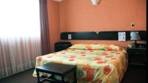 Ein Hotelzimmer mit Bett, Nachttisch, Lampe und einem Fenster mit Vorhängen.