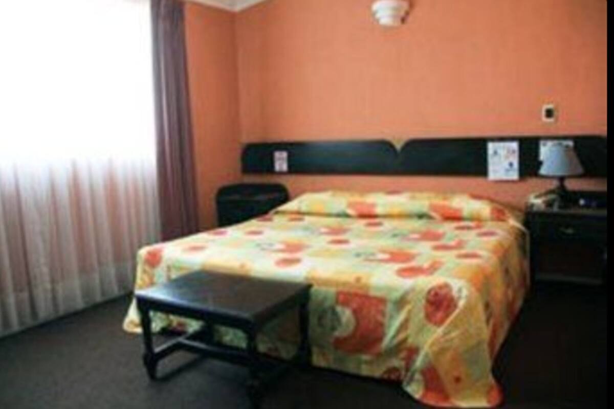 Ein Hotelzimmer mit Bett, Nachttisch, Lampe und einem Fenster mit Vorhängen.