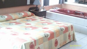 Ein Hotelzimmer mit Bett, Nachttisch, Lampe, einem Fenster mit Vorhängen und einer Badewanne.