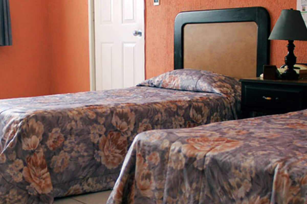 Ein Hotelzimmer mit zwei Betten, einem kleinen Tisch, einem Stuhl und einem Nachttisch mit Lampe.