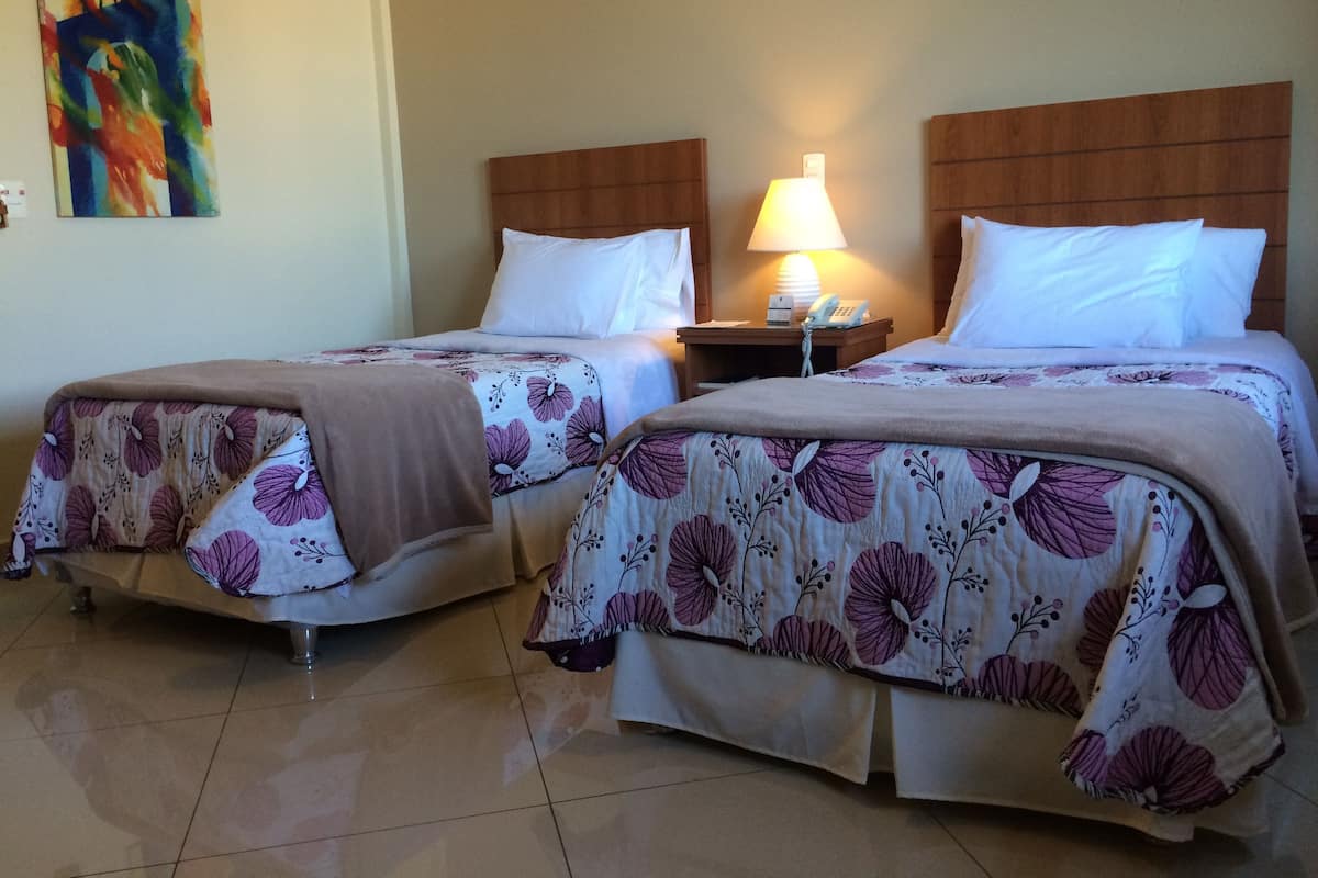 Two single beds with floral-patterned bedding, a nightstand with a lamp, and a colorful abstract painting on the wall.