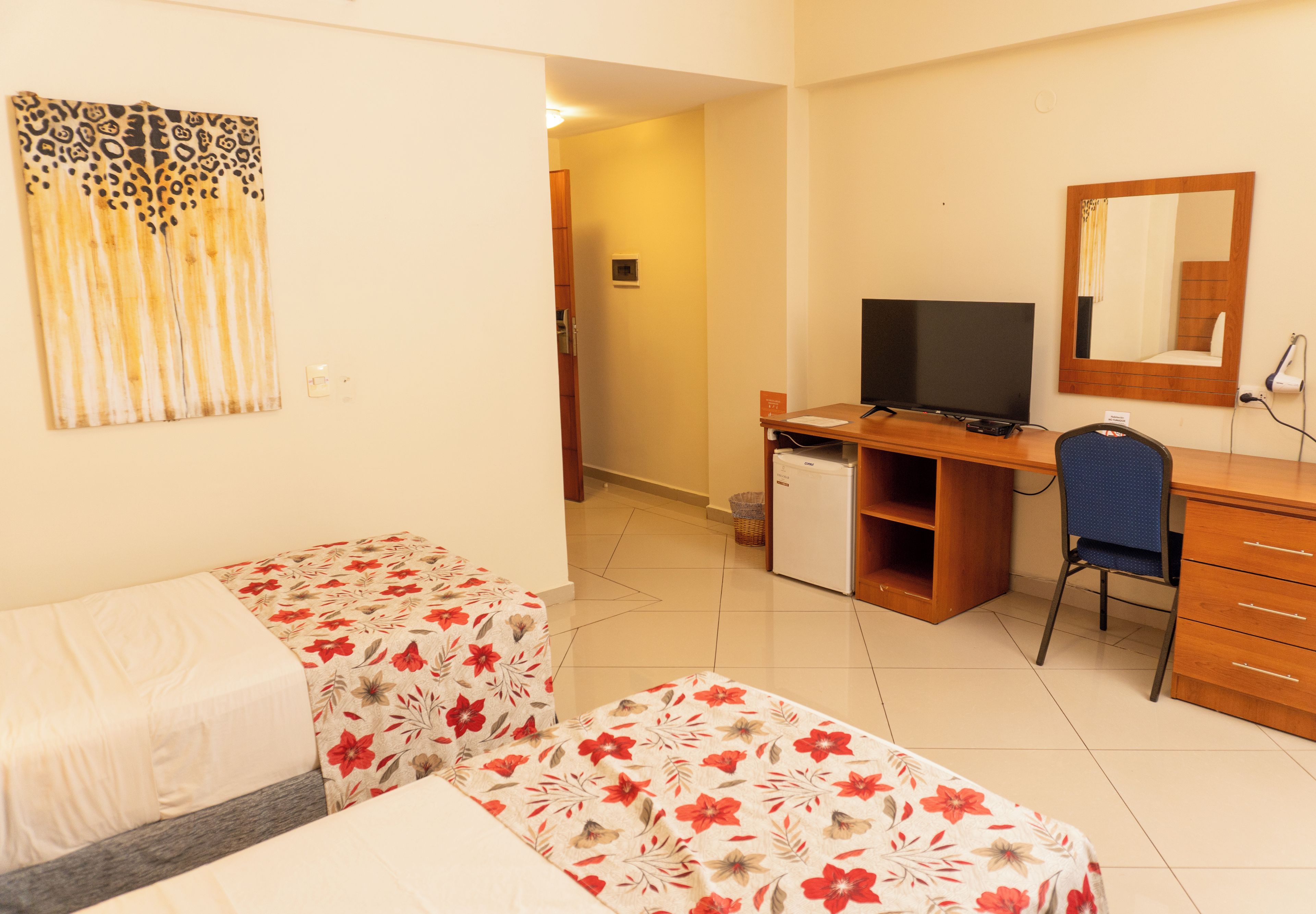A hotel room with two beds, a desk with a computer, a chair, and a television.