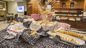 Un buffet proposant diverses viennoiseries et pâtisseries, un téléviseur diffusant des images en arrière-plan et un mur en bois orné de tableaux.