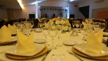 A banquet hall with round tables set for a formal event, complete with place settings, wine glasses, and a floral centerpiece.